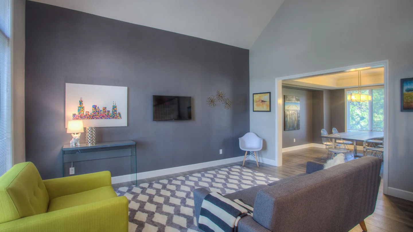 A lived-in living room: sectional sofa, green armchair, patterned rug, wall-mounted TV and a console table against a grey accent wall